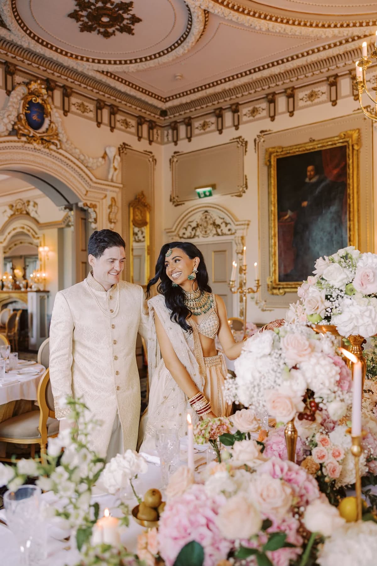 A couple in Indian wedding attire inside a luxury Irish reception room with floral tablescape